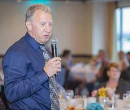 Chris Askin speaks into a mic to the guests gathered at the Atlantis for Margaret's retirement party.