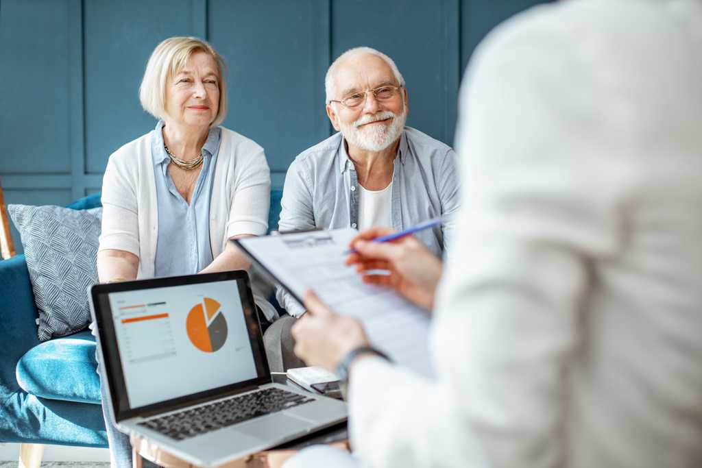 A senior couple meets with a professional woman, mostly off frame, who is looking at a computer as she speaks with them.