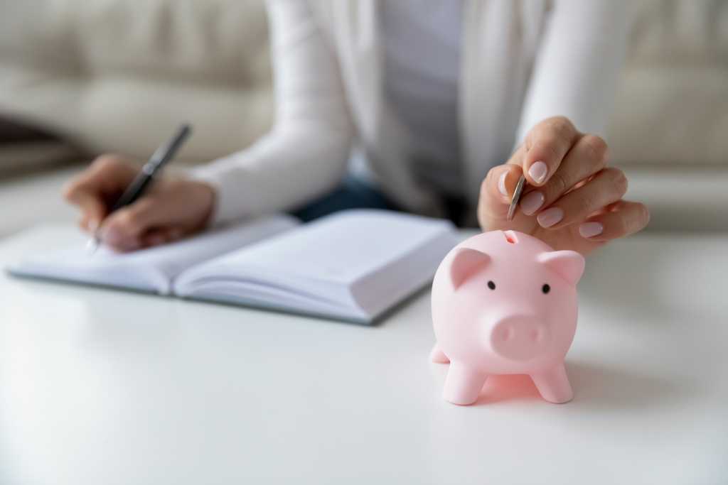 woman making notes and placing a penny in a piggy bank